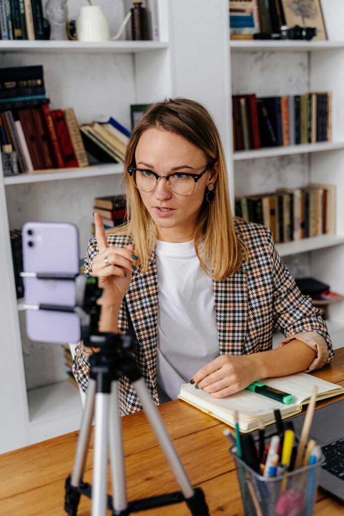 A woman in glasses delivers an online lesson using a smartphone. Modern teaching tools in a home setting.